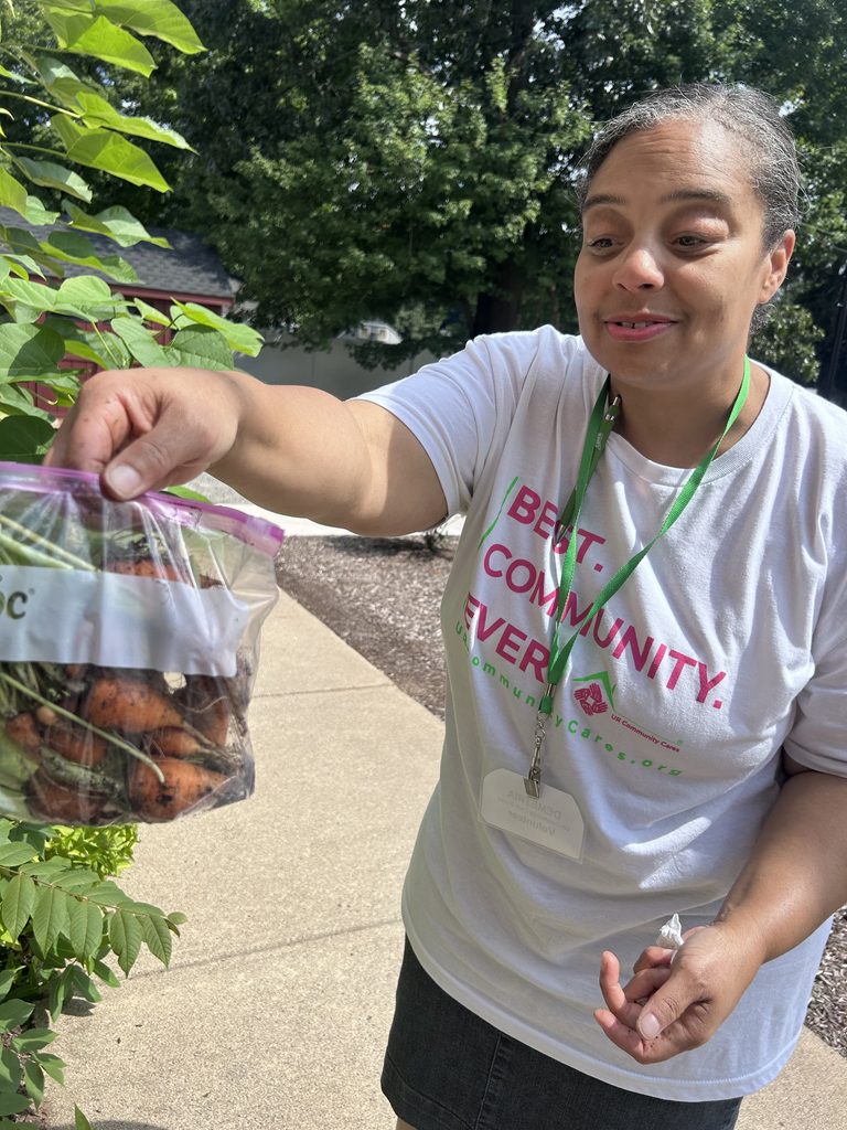 one person showing a bag of picked carrots from the community garden wearing  aUR Community Cares tshirt